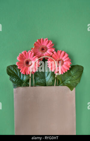 Coral Gerbera daisy flowers und Handwerk papper Einkaufstaschen auf grünem Papier Hintergrund, Frühling Verkauf Konzept Bild mit copy-Raum Stockfoto