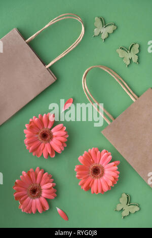 Coral Gerbera daisy flowers und Handwerk papper Einkaufstaschen auf grünem Papier Hintergrund, Frühling Verkauf Konzept Bild Stockfoto