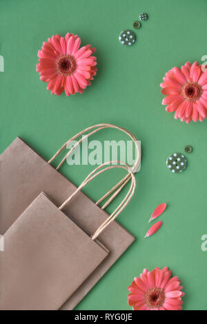 Coral Gerbera daisy flowers und Handwerk papper Einkaufstaschen auf grünem Papier Hintergrund, Frühling Verkauf Konzept Bild mit copy-Raum Stockfoto