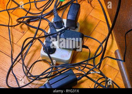 Kabelsalat und Batterie lädt auf parquete Stock. Haushaltsgeräte. Kabel Unordnung im heimischen Raum. Stockfoto