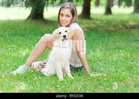 Junge Frau mit ihr spielen Golden Retriever Welpen im Freien Stockfoto