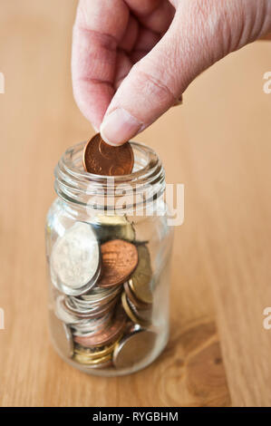 Hand eine Münze in eine Einsparung jar Stockfoto