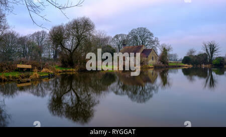 Sonnenaufgang über St Leonard's Kirche und Hartley Mauditt Teich, in der Nähe von Alton, in der South Downs National Park, Hampshire, Großbritannien Stockfoto