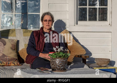 Eine ernsthafte reife Frau sitzt auf Ihrer Veranda Tee trinken im Morgenlicht der ländlichen Shenandoah Valley, Virginia, USA. Stockfoto