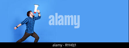 Bärtige Hipster in ein Megaphon auf blauem Hintergrund schreien, Panoramic Image mit Platz für Text Stockfoto