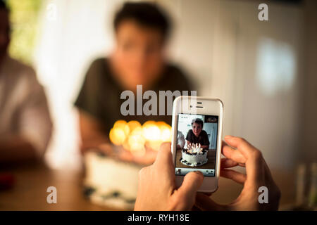 Mutter nimmt ein Foto von ihrem Sohn und seinen Geburtstag Kuchen auf Ihr Handy. Stockfoto