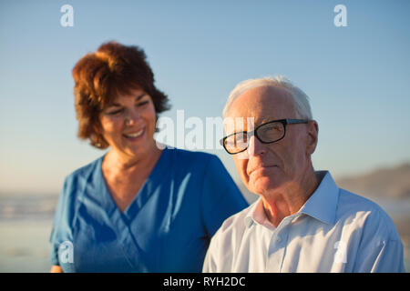 Portrait von ein älterer Mann am Strand mit einer weiblichen Pflegekraft. Stockfoto