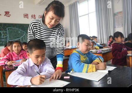 (190313) - RUILI, 13. März 2019 (Xinhua) - Lehrer Wang Deyu bietet Orientierungshilfen eine Studentin aus Myanmar an Yinjing Yinjing Grundschule im Dorf in Ruili, im Südwesten der chinesischen Provinz Yunnan, 8. März 2019. Yinjing Primary School ist an der Grenze zu China und Myanmar entfernt und hat insgesamt 135 Studierende, darunter 36 Studierende aus Myanmar. Ruili, einer Stadt an der Grenze China-Myanmar, ist ein wichtiges Land Hafen im Südwesten Chinas. Eine berühmte chinesische Song namens 'Es ist ein schöner Ort" beschreibt die Schönheit der Stadt, mit seiner einzigartigen Landschaft und bunte Folklore. Stockfoto