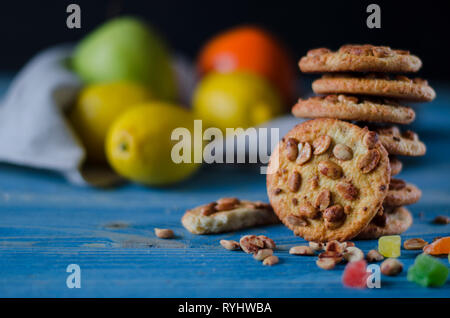 Runde orange Biscuits mit bunten kandierte Früchte und ein Stück saftige Orange liegen auf einem Holztisch. Nahaufnahme Stockfoto