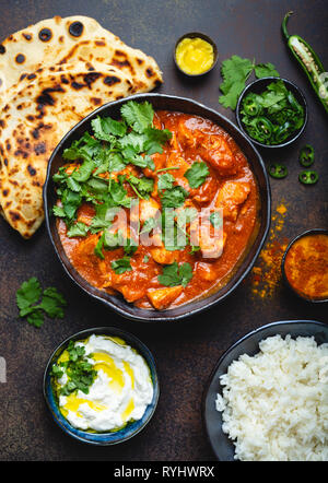 Traditionelle indische dish Chicken Tikka Masala mit würzigem Curry Fleisch in der Schüssel, Basmati Reis, Brot Naan, Joghurt raita Soße auf rustikalen dunklen Hintergrund, t Stockfoto