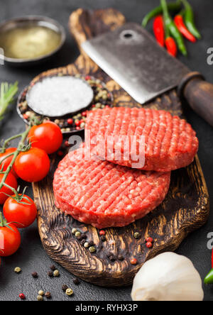 Frisches rohes Hackfleisch hausgemachte Landwirte Grill Rindfleisch Burger auf vintage Schneidbrett mit Gewürzen und Kräutern und Fleisch Hatchet auf schwarzem Hintergrund. Stockfoto