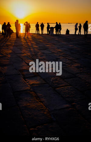 Silhouette von Menschen mit langen Schatten von Sonnenuntergang Sonne auf Dock Molo Audace in Triest, Italien Stockfoto