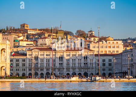 Blick von Molo Audace auf Piazza Unita d'Italia und Hügel mit Burg Castello di San Giusto auf Sonnenuntergang in Triest, Italien Stockfoto