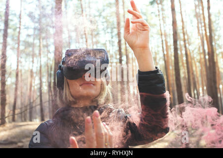 Eine Frau mit Virtual reality Brillen im Wald sieht Rauch Bomben. VR-Brille. Stockfoto