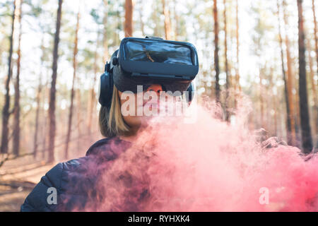 Eine Frau mit Virtual reality Brillen im Wald sieht Rauch Bomben. VR-Brille. Stockfoto