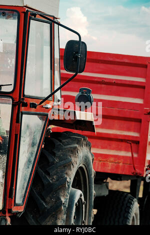 Alten roten landwirtschaftlichen Traktor mit Anhänger auf Schmutz Landstraße im Frühjahr am Nachmittag Stockfoto