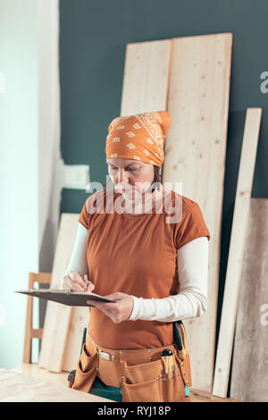 Selbständige Frau Carpenter Schreiben Hinweise zur Zwischenablage notepad Papier in kleinen Unternehmen Holzarbeiten workshop Stockfoto