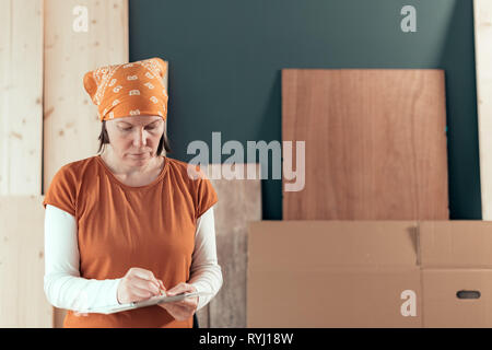 Selbständige Frau Carpenter Schreiben Hinweise zur Zwischenablage notepad Papier in kleinen Unternehmen Holzarbeiten workshop Stockfoto