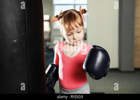 Kleine Mädchen in großen Boxhandschuhe Kampf mit Birne in der Turnhalle Stockfoto