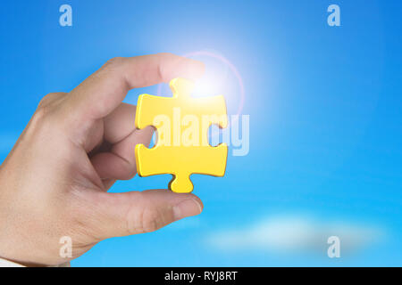 Hand mit gold Puzzle Stück mit blauer Himmel Sonnenlicht Hintergrund Stockfoto