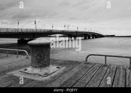 Schwarz-weiß Foto der Poller auf die Holzterrasse mit Brücke im Hintergrund - Wexford Irland Stockfoto