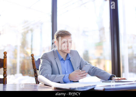 Junge Unternehmer im Cafe Tabelle und Prüfung Projekt sitzen. Blonde Mann, der smart Watch. Konzept des modernen Gadgets und Architektur Ausarbeitung roll Stockfoto