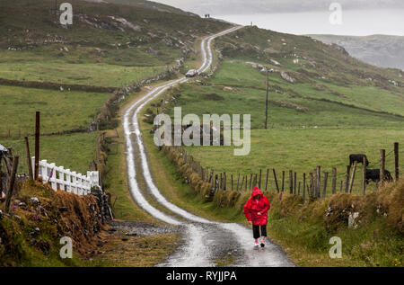 Dursey Island, Cork, Irland. 18 Juni, 2016 eine Frau geht auf der Hauptstraße an einem regnerischen Tag in der Gemeinde von Kilmichael auf dursey Island, Co Cork, ICH Stockfoto