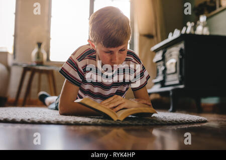 Zicklein liegend auf dem Boden und Lesen Buch. Junge Entspannen auf einem Teppich und ein Buch lesen zu Hause. Stockfoto