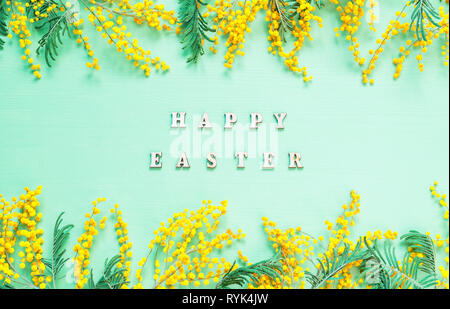 Ostern Hintergrund. Mimosen, Blumen und festliche Aufschrift Frohe Ostern - Urlaub Karte Stockfoto