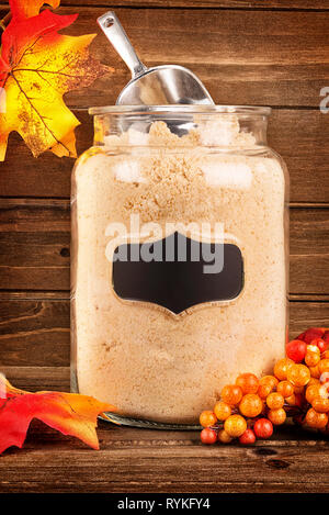 Granulierte ahorn Zucker in einem Glas aus Glas. Ahornblätter in der Dekoration und Holzbohlen im Hintergrund. Stockfoto