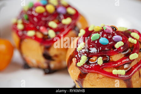 Close-up garniert Muffins mit den Belag von Süßigkeiten, Marmelade und dunkler Schokolade Sirup in weiße Platte. Stockfoto