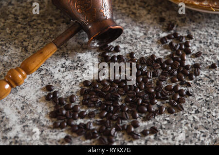 Cezve mit verschüttetem Kaffee Bohnen und Pfannkuchen mit gekochten Kartoffeln im Hintergrund Stockfoto
