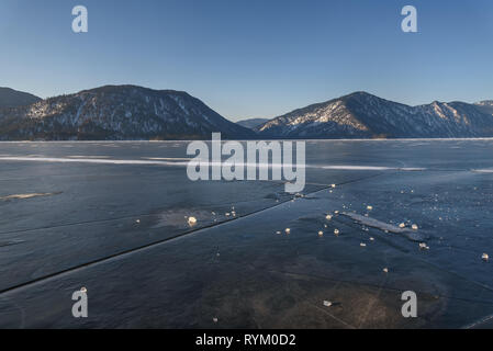 Schönen Winter Blick auf gefrorenen See mit Teletskoye Risse im Eis vor dem Hintergrund der Berge und blauer Himmel. Altai, Russland. Stockfoto