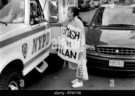 Die Anti-Klu-Klux-Klan-Rallyefrau überreicht dem New Yorker Polizist des NYPD eine Blume, der in seinem Polizeiwagen sitzt. Sie trägt ein Klan-Banner um ihren Hals. New York Juni 1990er Jahre Manhattan New York USA Juni 1999 HOMER SYKES Stockfoto