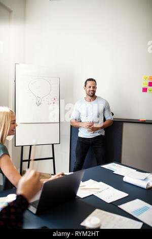 Lächelnd Manager im Gespräch mit Mitarbeiter sitzen um einen Tisch und eine kreative Whiteboard-Präsentation Stockfoto
