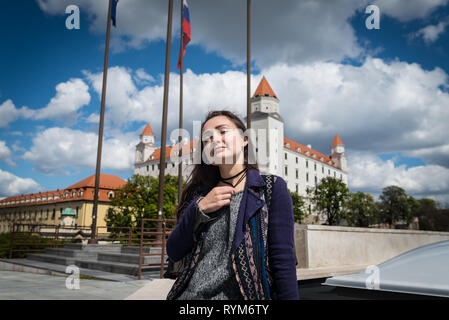 Junge Frau sitzt auf Platz mit Blick auf die Burg. Schöne Mädchen genießen Urlaub auf dem Hintergrund der wichtigsten städtischen Gebäude in Bratislava, Slowakei. Stockfoto