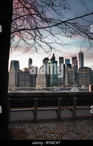 Malerischer Blick von Brooklyn auf Manhattan Wolkenkratzer in Abend mal in New York, USA. Bänke am Flußufer auf dem Hintergrund der Innenstadt und den Sonnenuntergang. Stockfoto