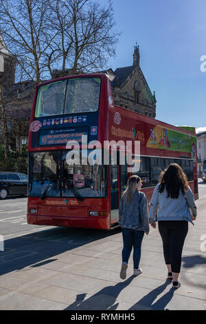 Zwei Fußgänger, die an einem roten Doppeldeckerbus mit offenem Oberdeck vorbeilaufen, York, North Yorkshire, England, Großbritannien. Stockfoto