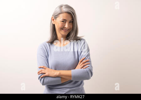 Schöne grauhaarige Frau mit verschränkten Armen Stockfoto