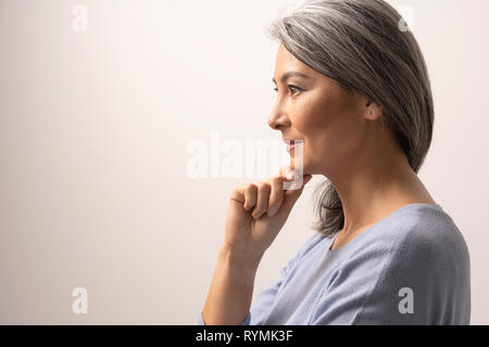 Nachdenkliche Frau berührt das Kinn und lächelt leicht Stockfoto