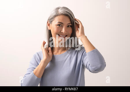 Lächelnd asiatische Frau berührt ihr graues Haar Stockfoto