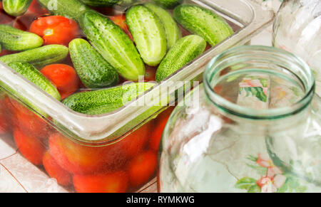 Vorbereitung von Pickles für den Winter. Tomaten und Gurken in Salzlake und Gläser auf dem Tisch. Stockfoto