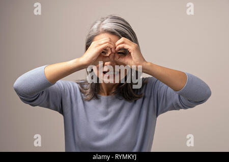 Asiatische reife Frau ist ok Geste wie ein Fernglas. Stockfoto