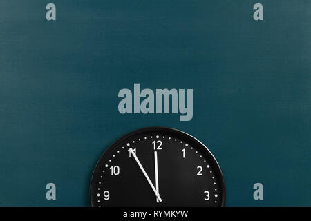 Runde Wanduhr mit 5 Minuten bis Mitternacht am Schwarzen Brett Hintergrund Stockfoto