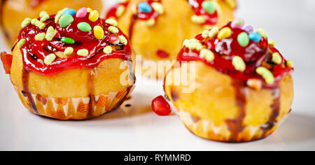 Close-up garniert Muffins mit den Belag von Süßigkeiten, Marmelade und dunkler Schokolade Sirup in Weiß Fach. Stockfoto