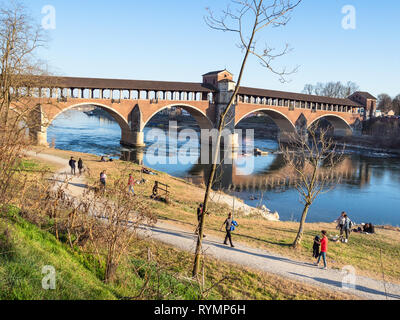 PAVIA, Italien - 22. FEBRUAR 2019: Leute gehen am Strand von Ticino und Blick auf Ponte Coperto (Brücke, Ponte Vecchio, Alte Brücke) in Pavia Stockfoto