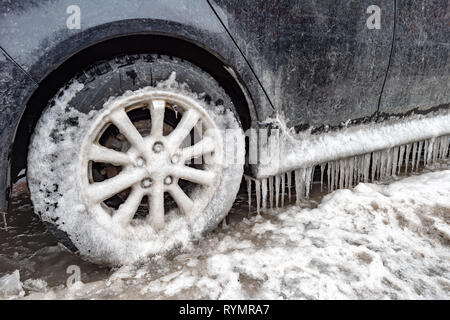 Eisansammlung und Eiszapfen auf einem Auto und close-up auf einem Rad, in Montreal, Kanada. Stockfoto