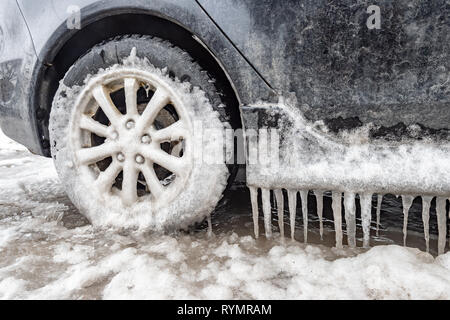 Eisansammlung und Eiszapfen auf einem Auto und close-up auf einem Rad, in Montreal, Kanada. Stockfoto