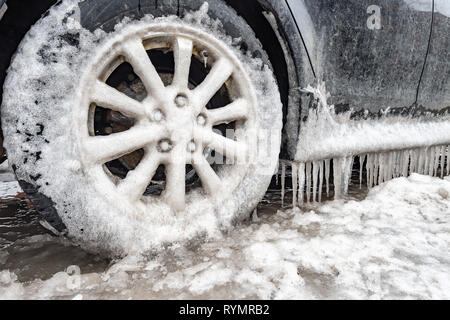 Eisansammlung und Eiszapfen auf einem Auto und close-up auf einem Rad, in Montreal, Kanada. Stockfoto