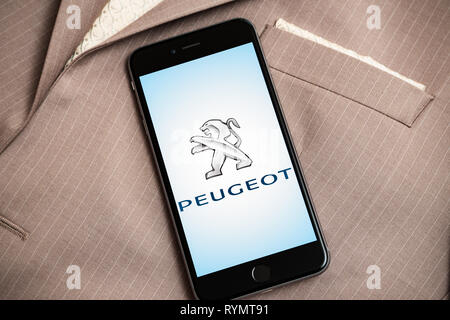 Schwarzes iPhone mit Logo der französischen Autofabrik Peugeot auf dem Bildschirm. Car Factory - Symbol. Anzug auf dem Hintergrund Stockfoto